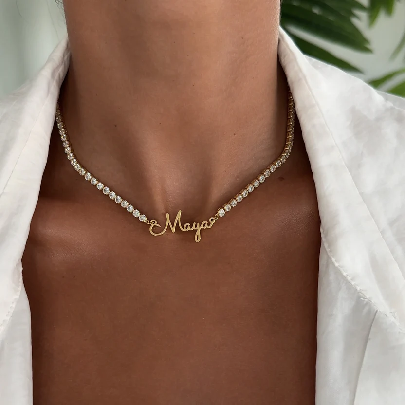 A close-up of a woman wearing a sparkling diamond tennis necklace with a gold script nameplate reading "Maya," highlighting 2025 jewellery trends in personalised jewellery.