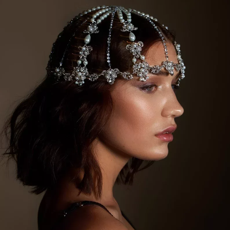 A woman wearing a stunning regal headpiece adorned with pearls and intricate jeweled details, showcasing one of the top 2025 jewellery trends.