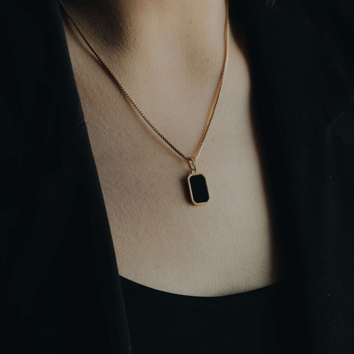 Close-up of a woman wearing a gold necklace with a rectangular black gemstone pendant, showcasing elegant black gemstone jewellery.