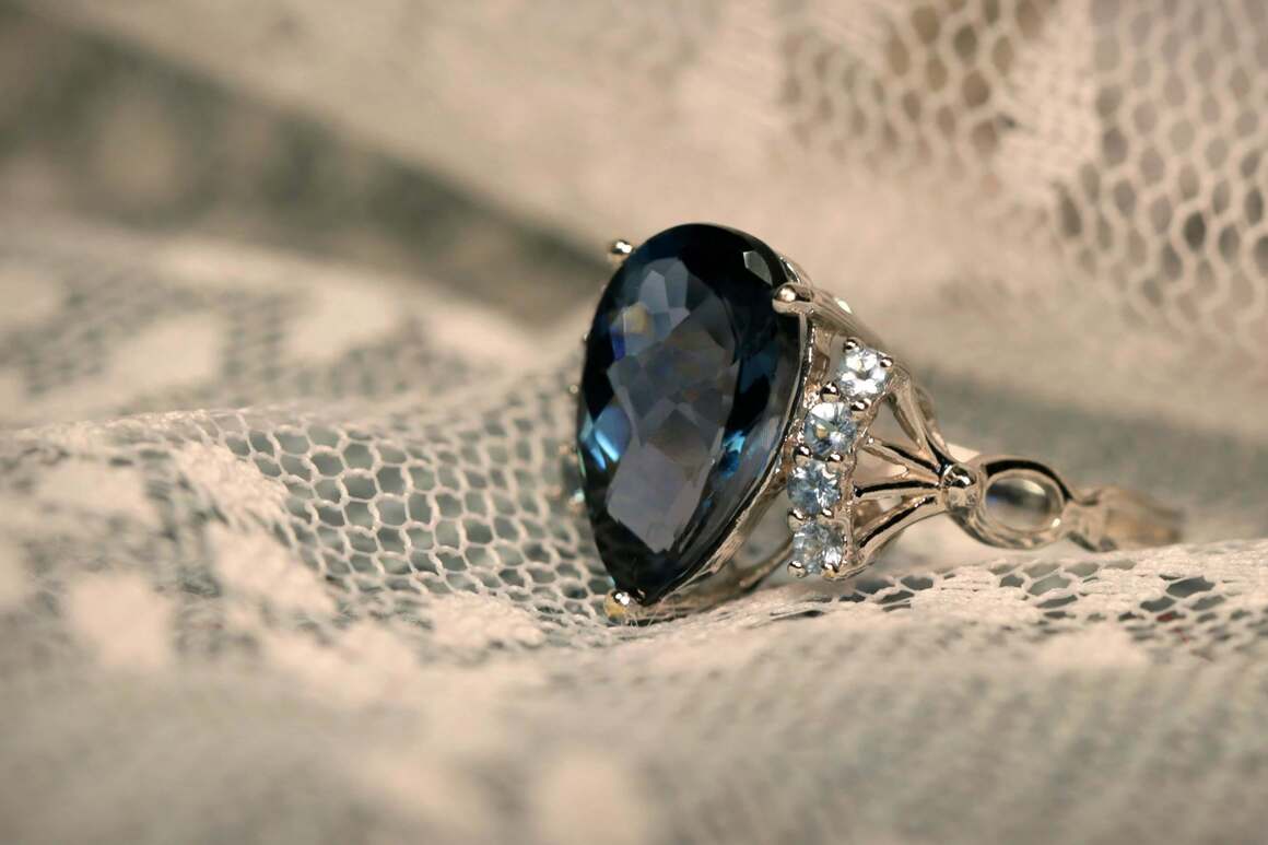 A close-up of a gemstone engagement ring featuring a large pear-shaped blue sapphire surrounded by smaller diamonds, highlighting 2025 jewellery trends.