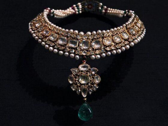 An ornate Indian kundan necklace featuring diamonds, gold, rows of pearls, and a central emerald drop, highlighting the pearl as the June birthstone.