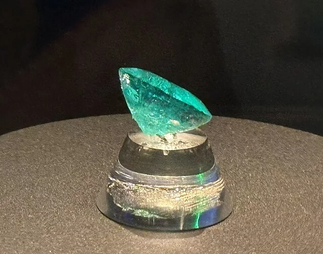 The Carolina Emperor emerald, a large uncut green emerald crystal displayed on a clear stand.