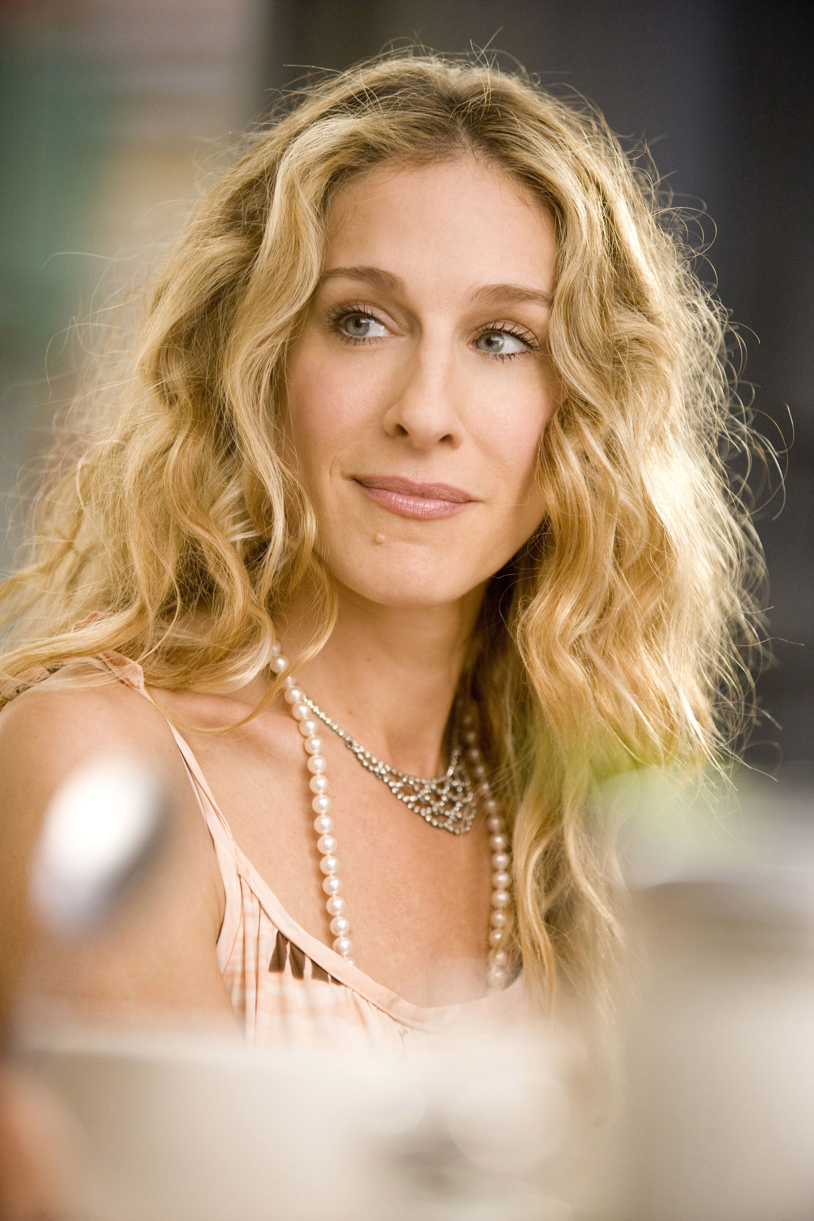 Sarah Jessica Parker in Sex and the City wearing a delicate pink dress, layered with a classic long pearl necklace and a sparkling statement necklace, highlighting the modern appeal of pearls on screen.