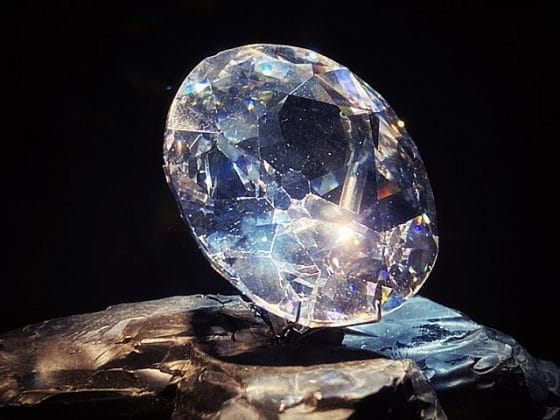 The Koh-i-Noor Diamond, one of the precious gemstones. A large, faceted diamond replica on display, illuminated dramatically against a dark background.