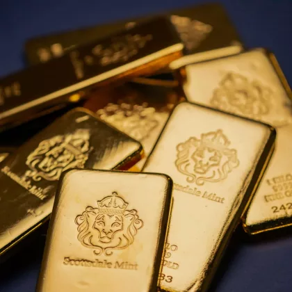 Several gold bars from Scottsdale Mint stacked on a dark blue background, displaying lion head emblems and mint markings.