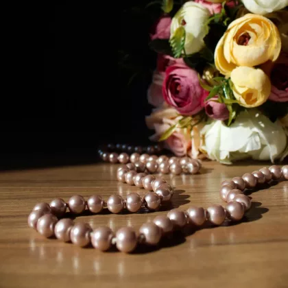 A strand of pink pearls, the classic June birthstone, displayed on a wooden surface with a bouquet of pastel flowers in the background.