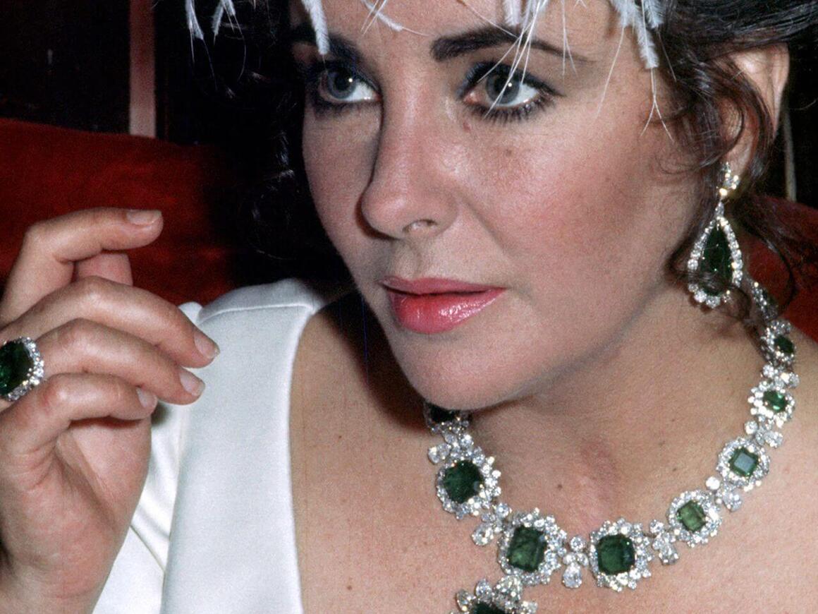 Elizabeth Taylor wearing her iconic emeralds: a Bulgari emerald and diamond necklace, matching earrings, and an emerald ring.
