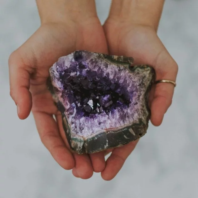 A pair of hands gently holding a raw amethyst geode, displaying vibrant purple crystals with deep and light hues, perfectly illustrating Purple Gemstones: Amethyst.