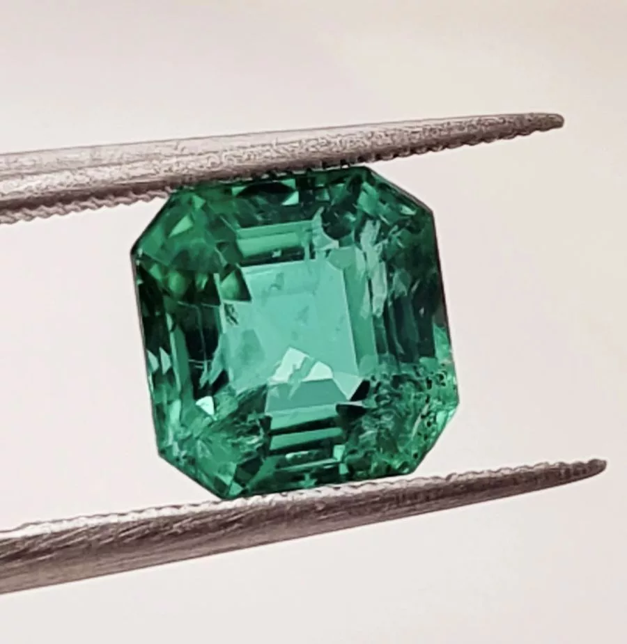 Close-up of a vivid green emerald gemstone held by tweezers, highlighting its clarity and cut—an ideal choice for gemstone investments.