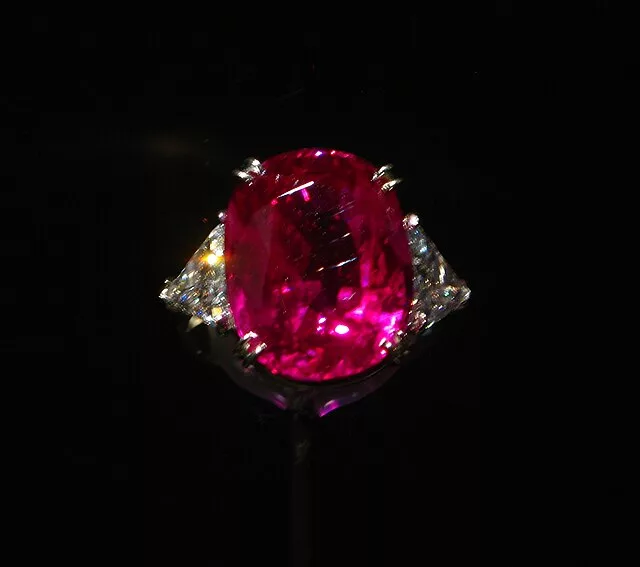 A dazzling oval-cut ruby ring, the vivid red gemstone flanked by sparkling diamonds, set against a dark background, beautifully representing the July birthstone.
