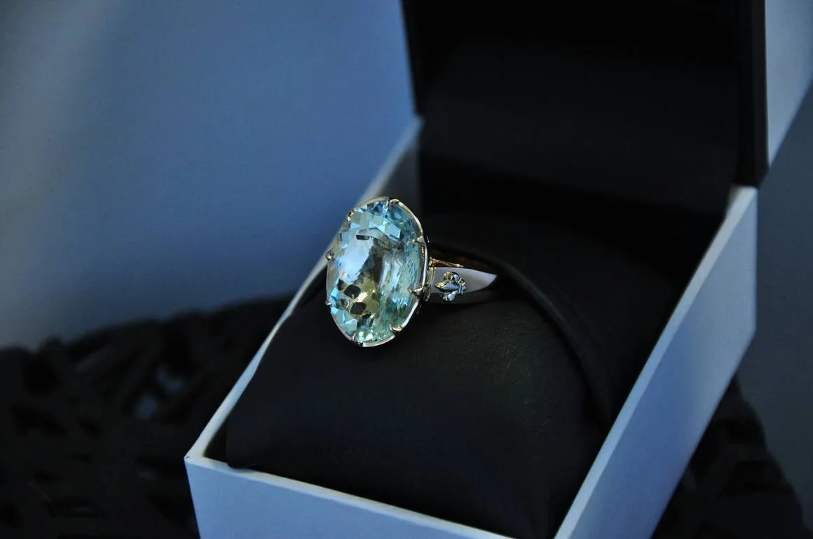 A close-up of a stunning aquamarine ring with a large, oval-cut pale blue gemstone set in a silver band, elegantly displayed in a black ring box, representing March birthstones aquamarine.