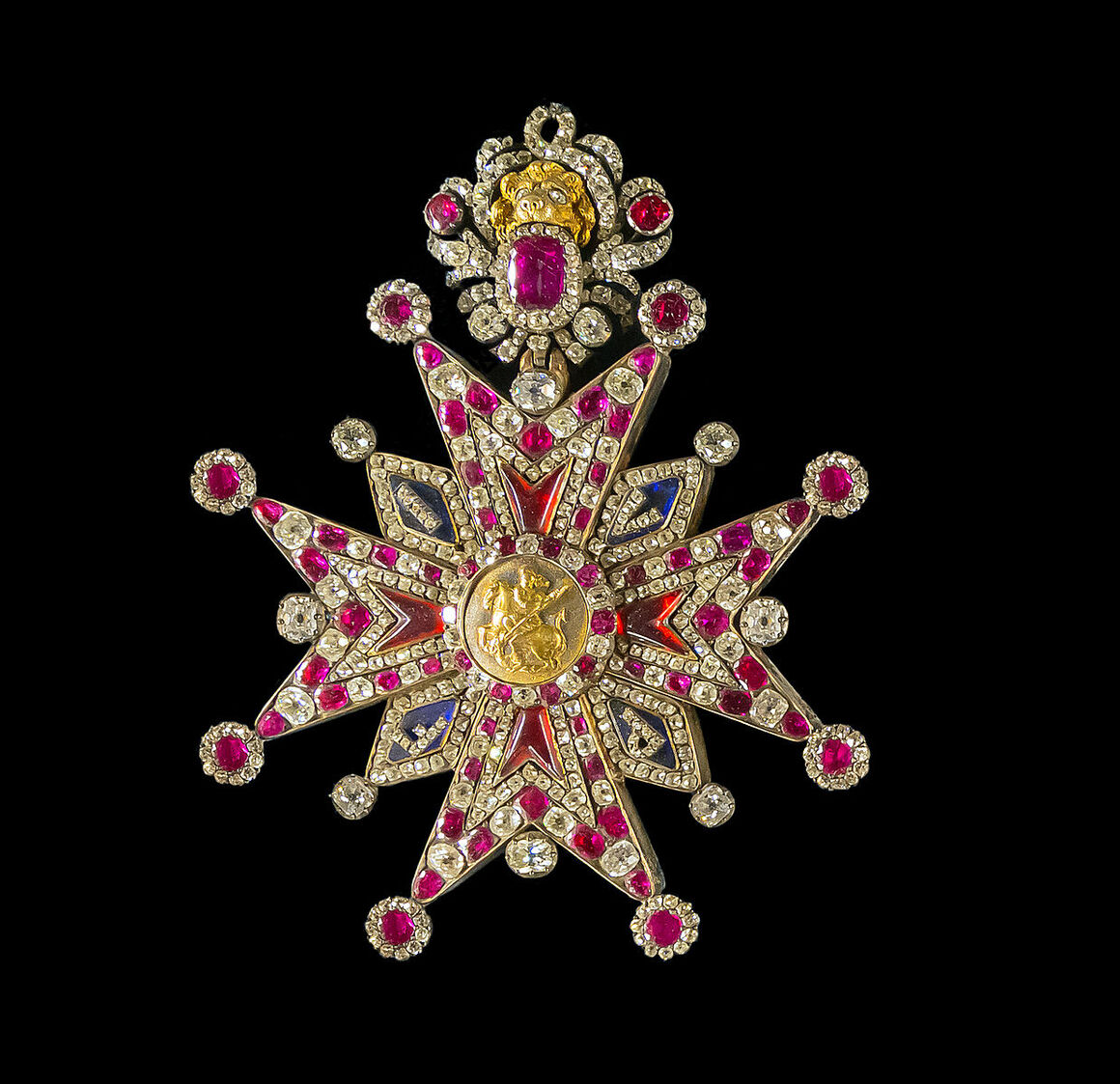An ornate star-shaped pendant encrusted with rubies, diamonds, and gold accents, featuring a central gold medallion and intricate detailing, set against a black background.