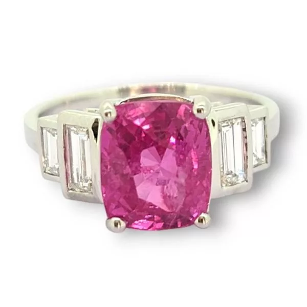 A white gold ring featuring a large, cushion-cut pink sapphire at the center, flanked by four baguette-cut white diamonds on each side, exemplifying the elegance of pink gemstones and the brilliance of pink sapphire.