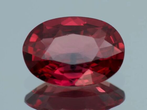 A vivid, faceted oval-cut ruby gemstone with deep red color and excellent clarity, reflecting light on a smooth surface, showcasing the beauty of rubies.
