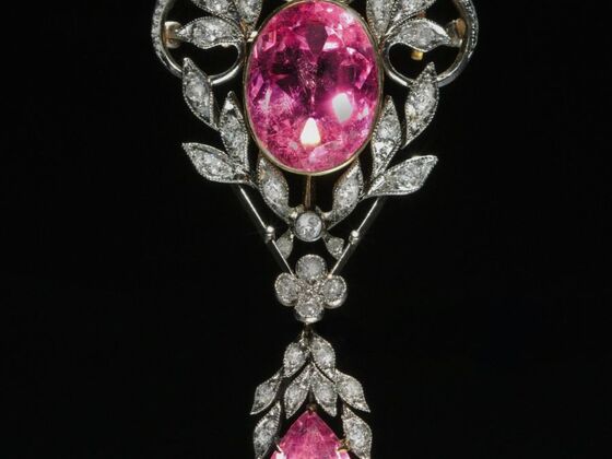 An ornate Art Nouveau brooch featuring an oval pink gemstone and a pear-shaped pink tourmaline, both surrounded by intricate diamond-set leaf motifs— , exemplifying the beauty of pink gemstones.