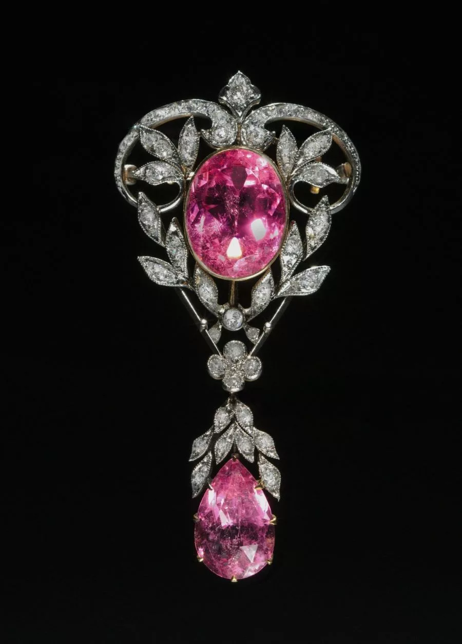 An ornate Art Nouveau brooch featuring an oval pink gemstone and a pear-shaped pink tourmaline, both surrounded by intricate diamond-set leaf motifs— , exemplifying the beauty of pink gemstones.
