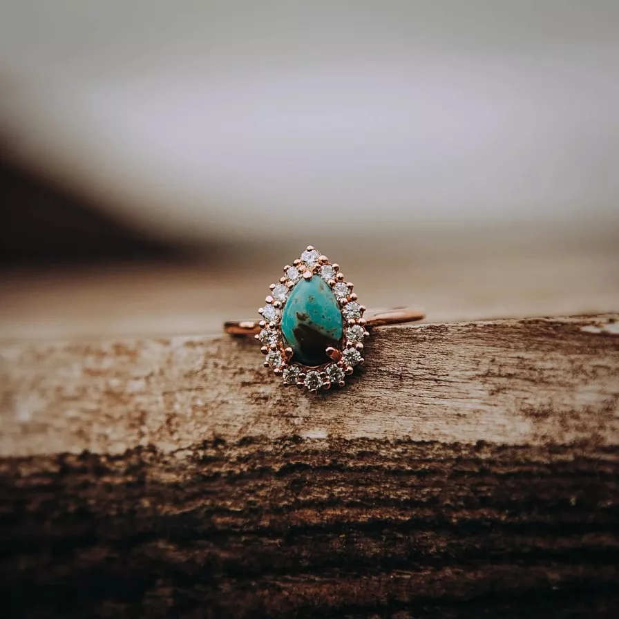 A pear-shaped turquoise gemstone ring surrounded by a halo of sparkling diamonds, set in a delicate rose gold band, beautifully illustrating the appeal of semi-precious gemstones.
