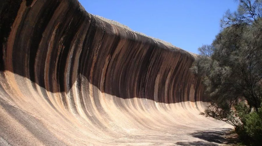 The striking curved formation of Wave Rock in Western Australia, with dramatic vertical stripes and a smooth, wave-like surface under a clear blue sky—an iconic example of Geological and Mineral Destinations in Australia.