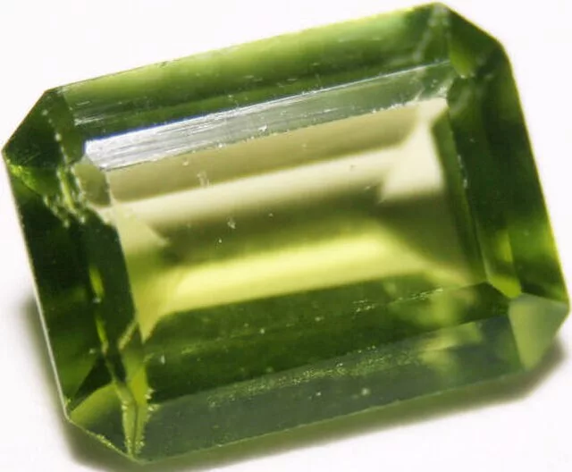 A faceted, vibrant green peridot gemstone cut in an emerald shape, displaying bright clarity and rich color characteristic of august birthstones.