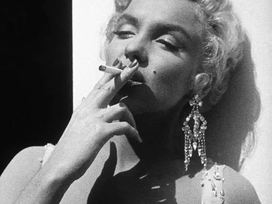 Black and white portrait of Marilyn Monroe in a glamorous dress, smoking a cigarette, wearing sparkling chandelier earrings and a glamorous look highlighting her style and allure.