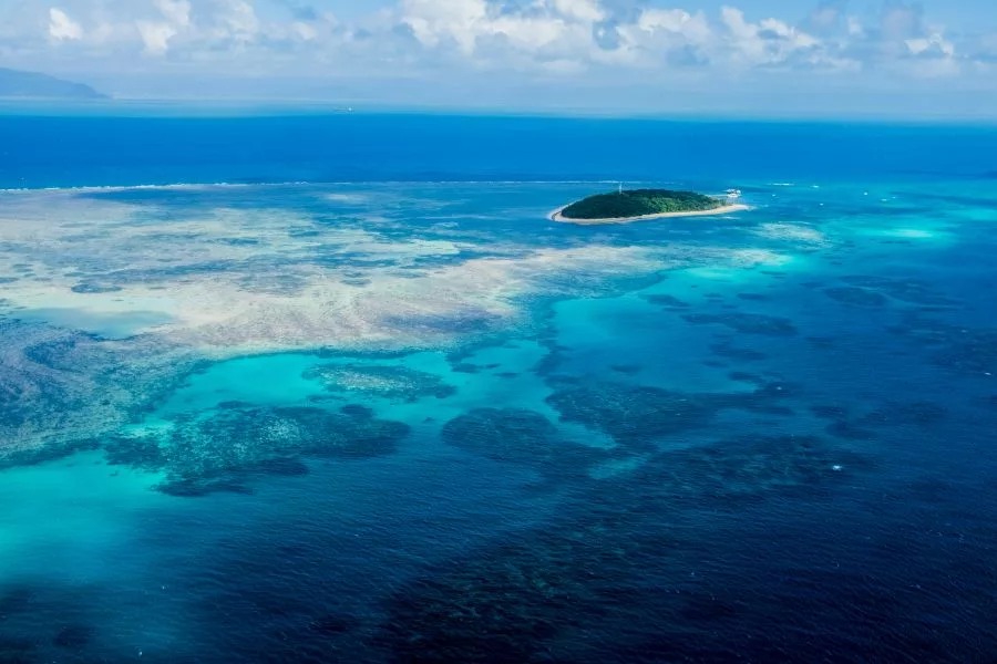 Aerial view of a tropical island surrounded by vibrant coral reefs in the Great Barrier Reef, one of the premier geological and mineral destinations in Australia.