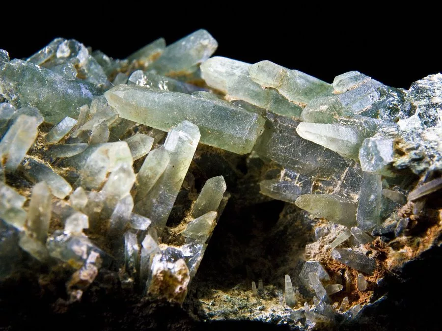 A cluster of translucent green prasiolite crystals, also known as green quartz, with elongated hexagonal formations and subtle earthy inclusions, highlighting the natural beauty and mineral structure of prasiolite.