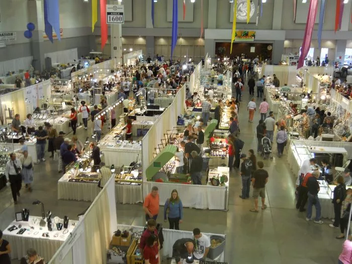 A bustling exhibition hall at the Tucson Gem & Mineral Show, filled with gemstone and mineral booths, attendees, and jewelers, showcasing the Global Gemstone Trade.