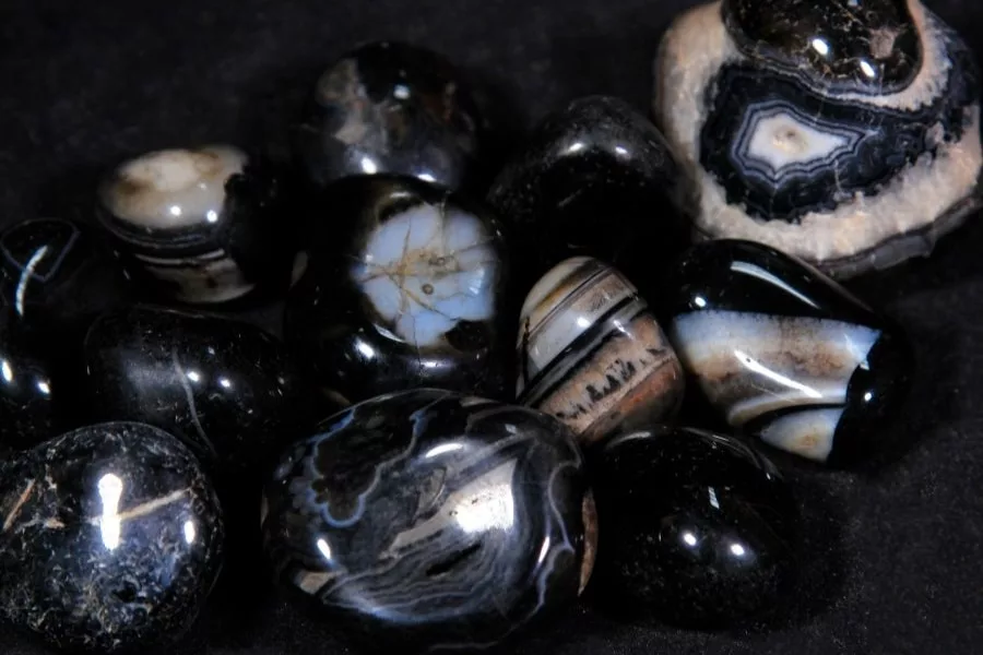 A collection of polished black onyx stones with distinctive white and gray banding, displaying the characteristic glossy surface and layered patterns of onyx.