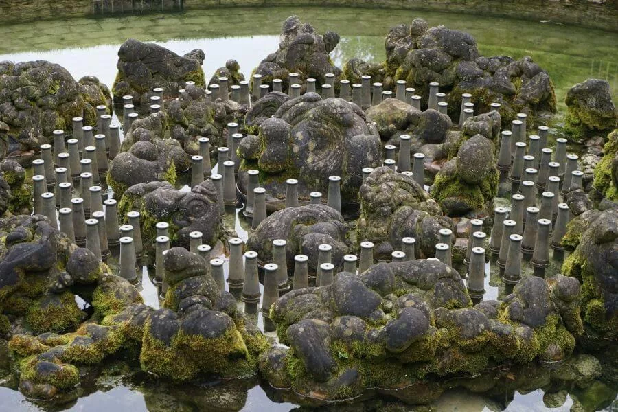 Moss-covered Gogottes at Versailles surrounded by water fountain nozzles in a shallow basin.