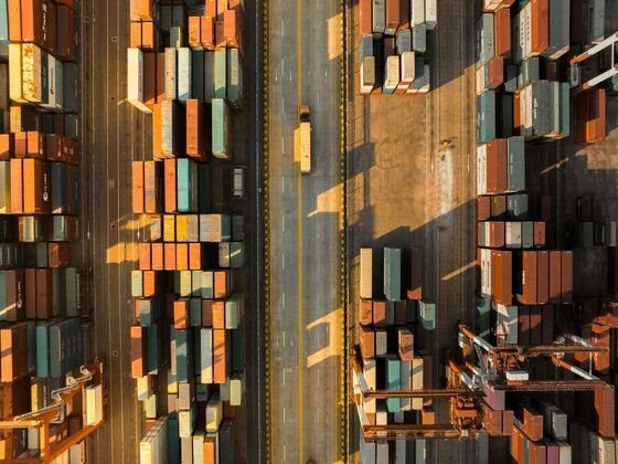 Aerial view of a shipping port with colorful cargo containers and a freight truck driving down the central road, illustrating global trade logistics.