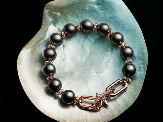 A luxurious bracelet featuring large black pearls, rose gold accents, and a bold, diamond-studded clasp, displayed on a shimmering shell—showcasing Tiffany & Co. in 2025 and the Tiffany & Co and Pharrell Williams Collab.