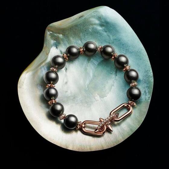 A luxurious bracelet featuring large black pearls, rose gold accents, and a bold, diamond-studded clasp, displayed on a shimmering shell—showcasing Tiffany & Co. in 2025 and the Tiffany & Co and Pharrell Williams Collab.