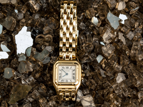 A gold Cartier Panthère watch displayed on a bed of reflective crystals, representing timeless luxury and the legacy of the Cartier family.