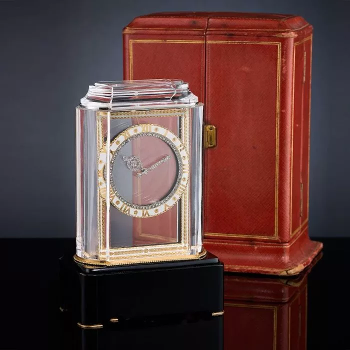 A luxurious Cartier mystery clock with rock crystal and gold accents, featuring transparent clock hands and a red decorative case, exemplifying innovation by the Cartier family.
